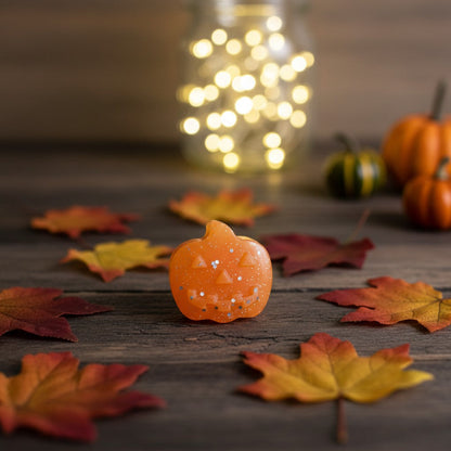 Absolute Whifs pumpkin shaped wax melt with glitter on a wooden table surrounded by autumn leaves and fairy lights