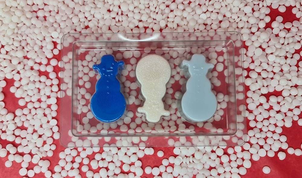 Snowmen scented wax melts in various colors on a background of white pellets.