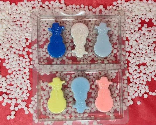 Colorful snowmen-shaped scented wax melts in a plastic tray, surrounded by white pellets on a red background.