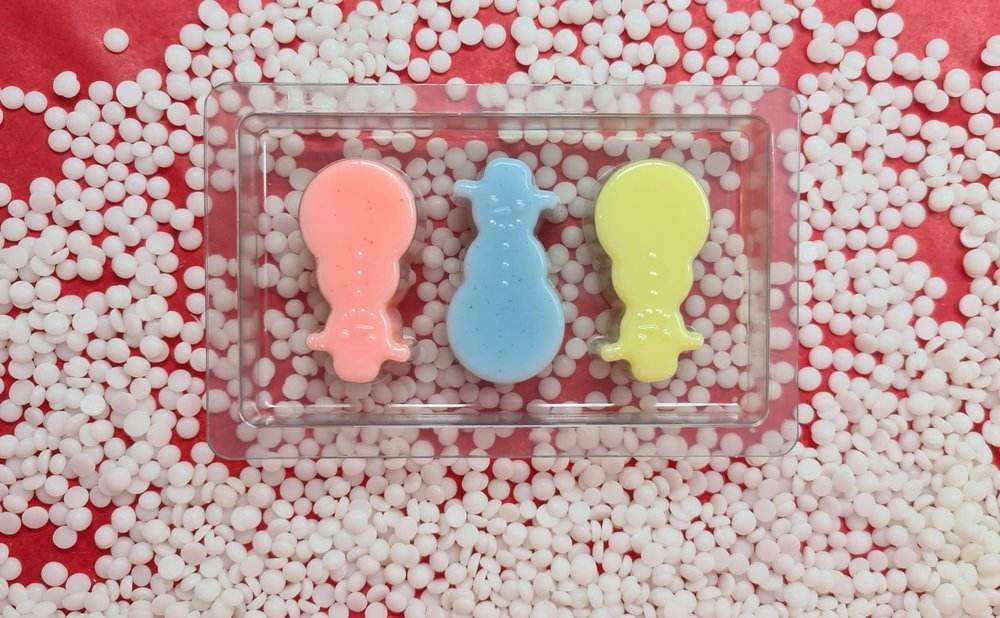 Snowmen shaped scented wax melts in pastel colors on a red and white background.