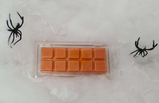 Orange pumpkin-themed wax melt clamshell with 10 segments, surrounded by Halloween decorations.